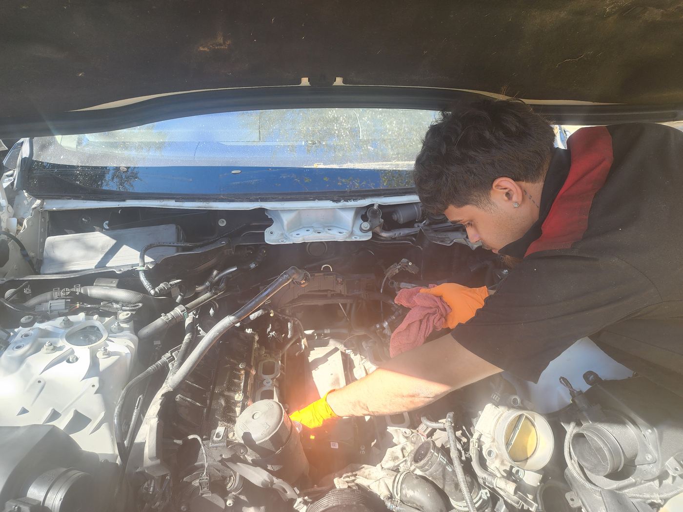 Certified mobile mechanic performing an engine repair under the hood at a customer's location